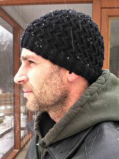 a man wearing a black knitted beanie looking out the window in the snow