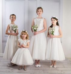 three girls in white dresses standing next to each other with flowers on their head and one girl wearing a flower crown