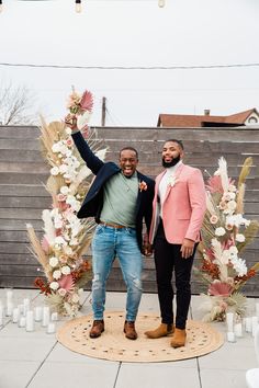 two men standing next to each other in front of a flower arch with flowers on it