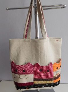 a handbag with two cats on it hanging from a metal rack next to a white wall