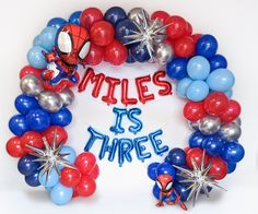 a wreath made out of balloons with the words miles is three written in red, white and blue