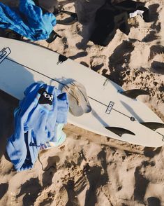 a white surfboard laying on top of a sandy beach next to blue towels and other items