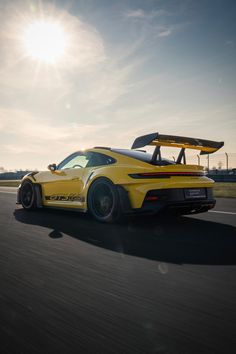 the yellow sports car is driving down the road in front of the sun on a sunny day