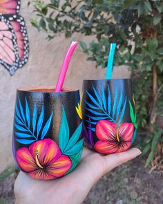 two hand painted cups with straws and flowers on them are held in front of a wall