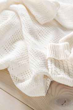 a white knitted blanket laying on top of a wooden floor next to a stuffed animal