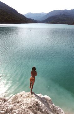 a woman standing on top of a rock next to a large body of blue water