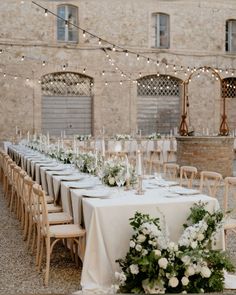 a long table with white flowers and greenery is set up in front of an old brick building