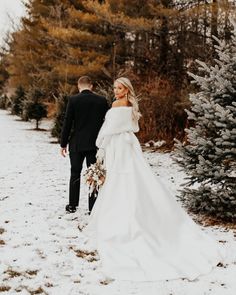 the bride and groom are walking through the snow in their winter wedding attire, holding hands