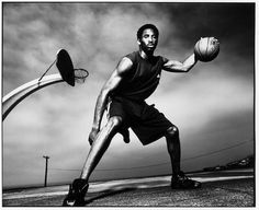 a man holding a basketball while standing on top of a street next to a pole