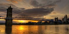 the sun is setting behind a bridge over water