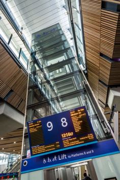 an airport sign hanging from the ceiling in front of a glass and wood building with stairs leading up to it