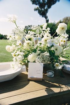 white flowers in a vase sitting on a table with a place card and plate next to it