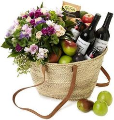 a basket filled with wine, fruit and flowers