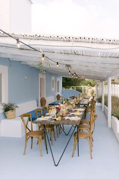 an outdoor dining area with blue walls and white trimmings on the ceiling, along with wooden chairs and tables