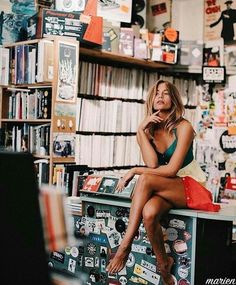 a woman sitting on top of a table in front of a book shelf filled with books