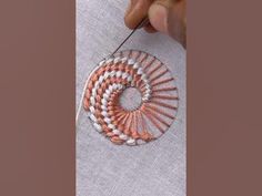 someone is stitching an orange and white piece of fabric with a small needle in the middle