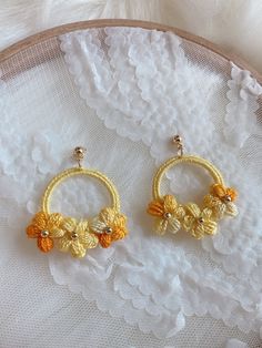 two pairs of yellow flower hoop earrings sitting on top of a white lace doily