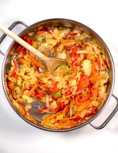 a large pot filled with vegetables on top of a white counter next to a wooden spoon