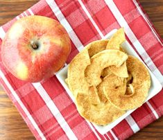 an apple and cinnamon roll on a red checkered table cloth next to the apple