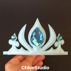 a tiara with blue and white crystals on the top is being held by a hand