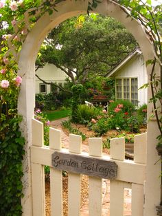 the garden cottage is surrounded by greenery and pink flowers, with a white picket fence