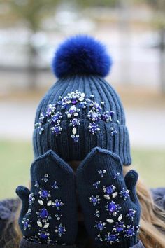 a woman wearing a blue hat and mittens with purple flowers on the front, while covering her face