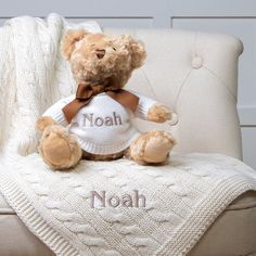 a brown teddy bear sitting on top of a white chair next to a blanket with the word noah written on it