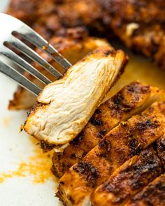 grilled chicken on a white plate with a fork in the foreground and another piece of meat sitting on top of it