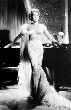 a woman in an evening dress standing next to a piano and holding her arms out