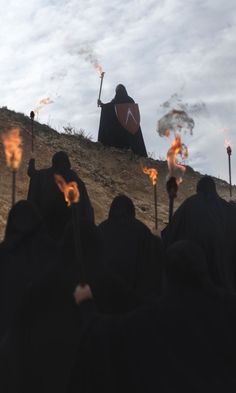 several people in black robes holding torches on a hill