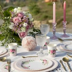 the table is set with pink roses and white china plates, silverware, and candles