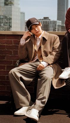 a man sitting on top of a bench next to a brick wall wearing a hat