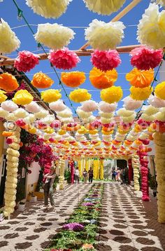 an outdoor walkway decorated with paper flowers and pom - poms in the sky