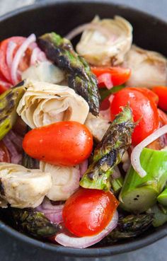 a salad with tomatoes, asparagus and other veggies in a black bowl