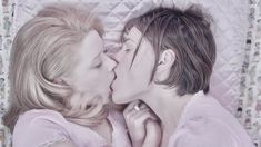 two women laying in bed kissing each other with their noses close to one another,