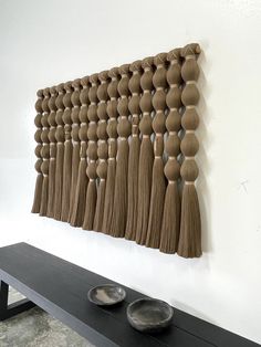 a wall hanging with tassels and bowls on the shelf in front of it