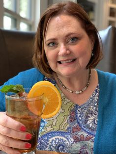 a woman sitting at a table with a glass of tea and an orange slice in her hand