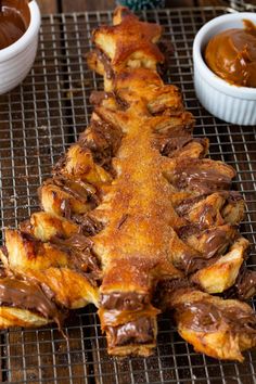 chocolate covered pastry sitting on top of a cooling rack next to bowls of dipping sauce