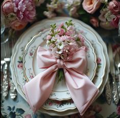 a pink bow on top of a plate with silverware and flowers in the background