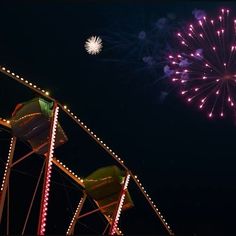 fireworks are lit up in the night sky above an amusement park ride