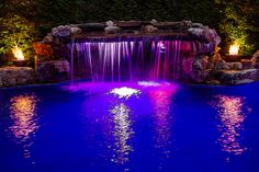 an illuminated pool with waterfall and water features lit up at night, surrounded by greenery