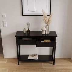 a black table with two vases on it and a white wall in the background