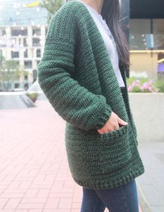 a woman wearing a green crochet cardigan is holding her hand in her pocket