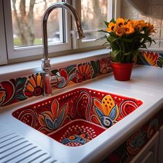 a kitchen sink with flowers in the window sill and painted tiles on the counter