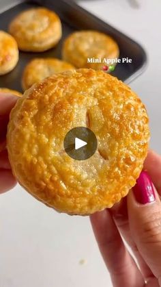 a person holding up a small pastry in front of some muffins on a pan