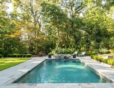 an outdoor swimming pool surrounded by greenery and trees in the back yard with lounge chairs