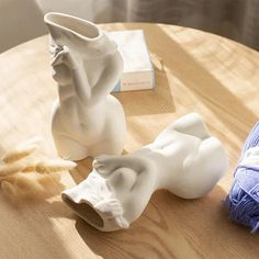 two white vases sitting on top of a wooden table next to a ball of yarn