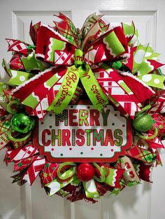 a merry christmas wreath hanging on a door with green and red decorations around the wreath