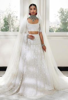 a woman standing in front of a window wearing a white wedding dress with sheer sleeves