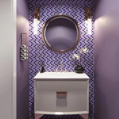 a bathroom with purple and white tiles on the walls, a round mirror above the sink